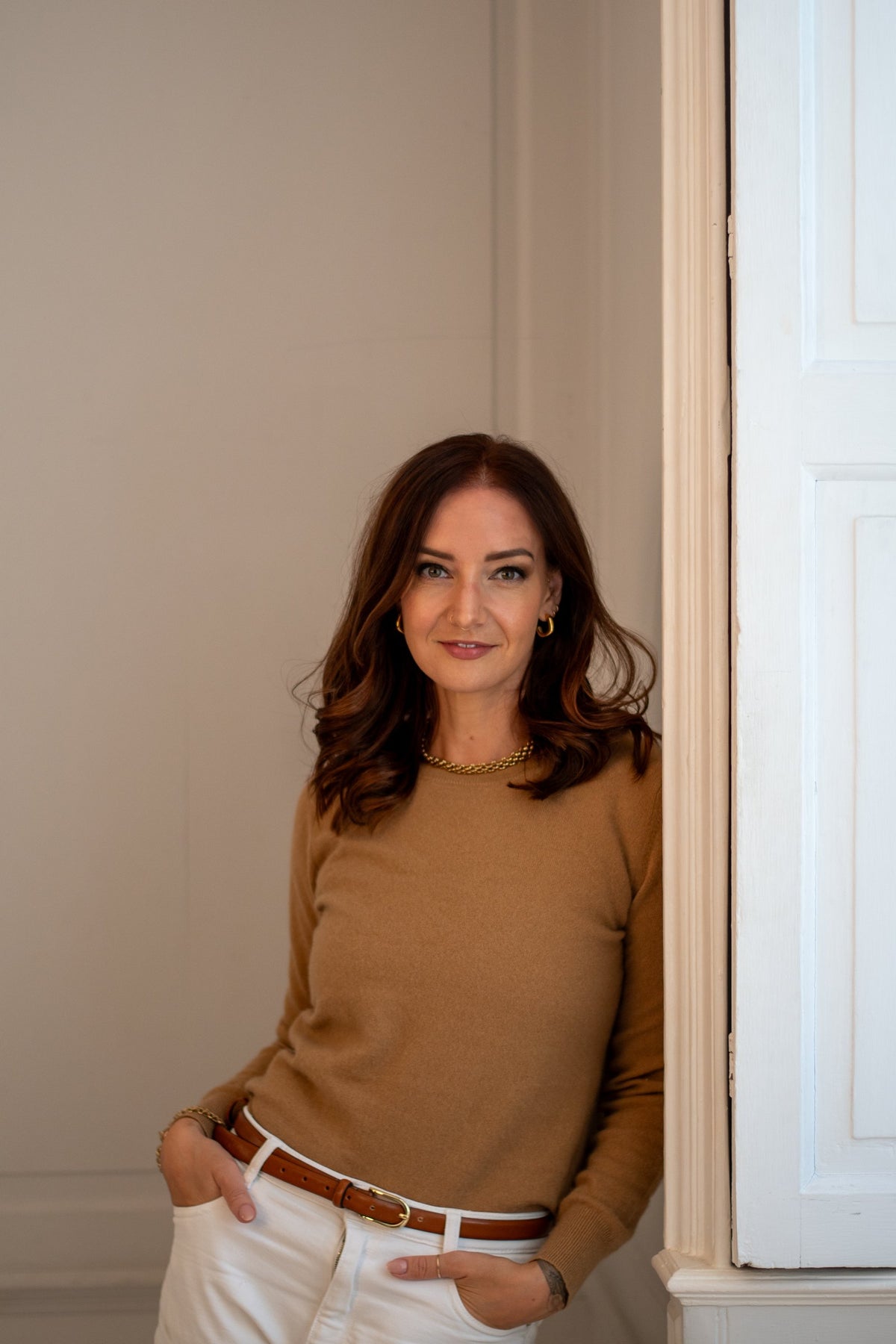 Lizz, founder of The Jewellery Edit, leaning in a doorway in a camel jumper