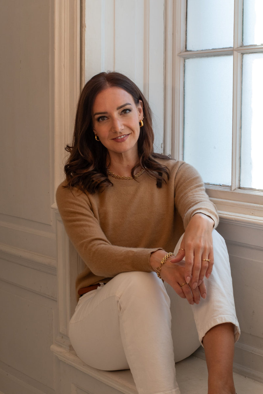 Lizz, founder of The Jewellery Edit, sitting in a window seat in a camel jumper