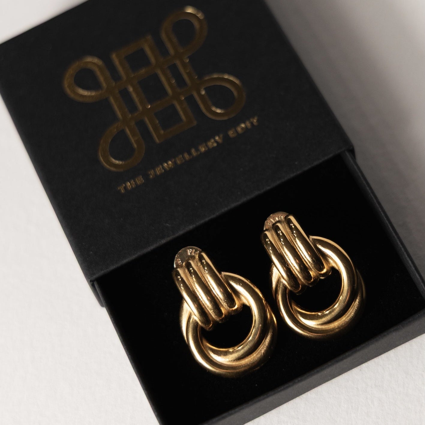 Gold hoop earrings in a black box with a brand logo on a white background