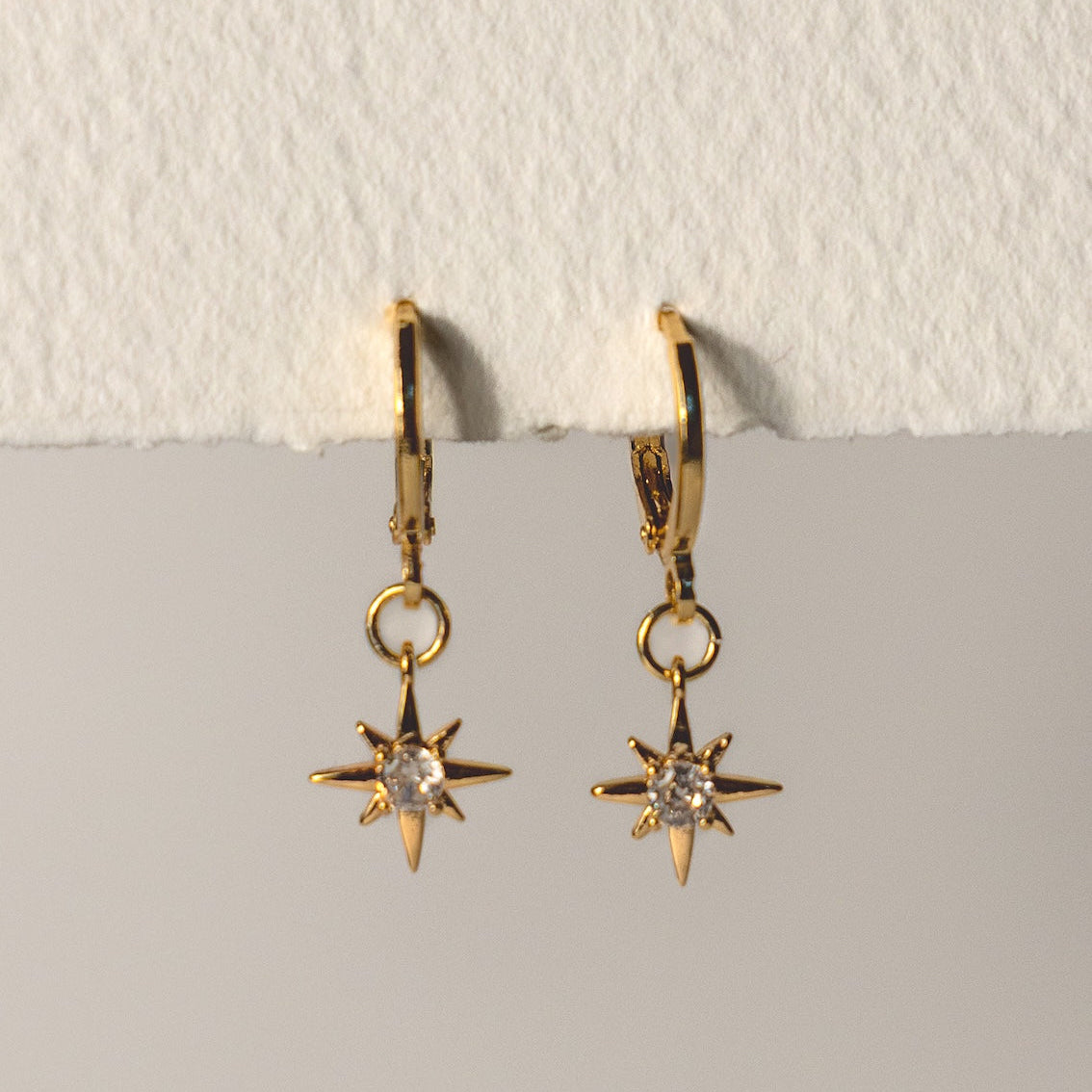 Gold star-shaped earrings with clear stones on a light gray background