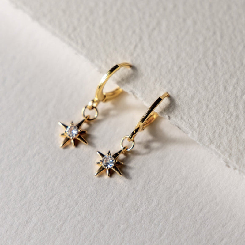 Gold hoop earrings with star designs on a textured white surface