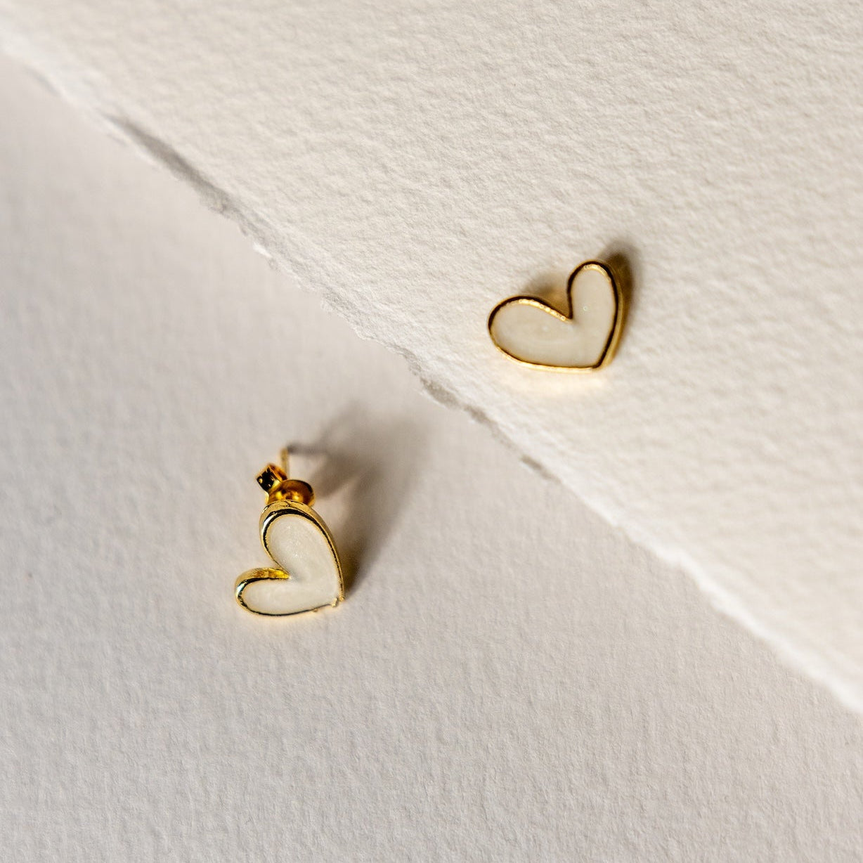 Heart-shaped gold earrings on a textured white surface