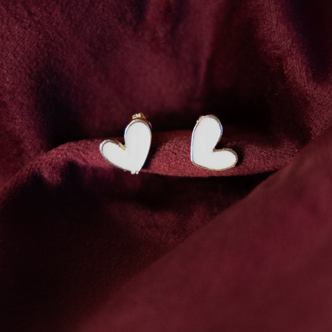 Heart-shaped earrings on a burgundy fabric background