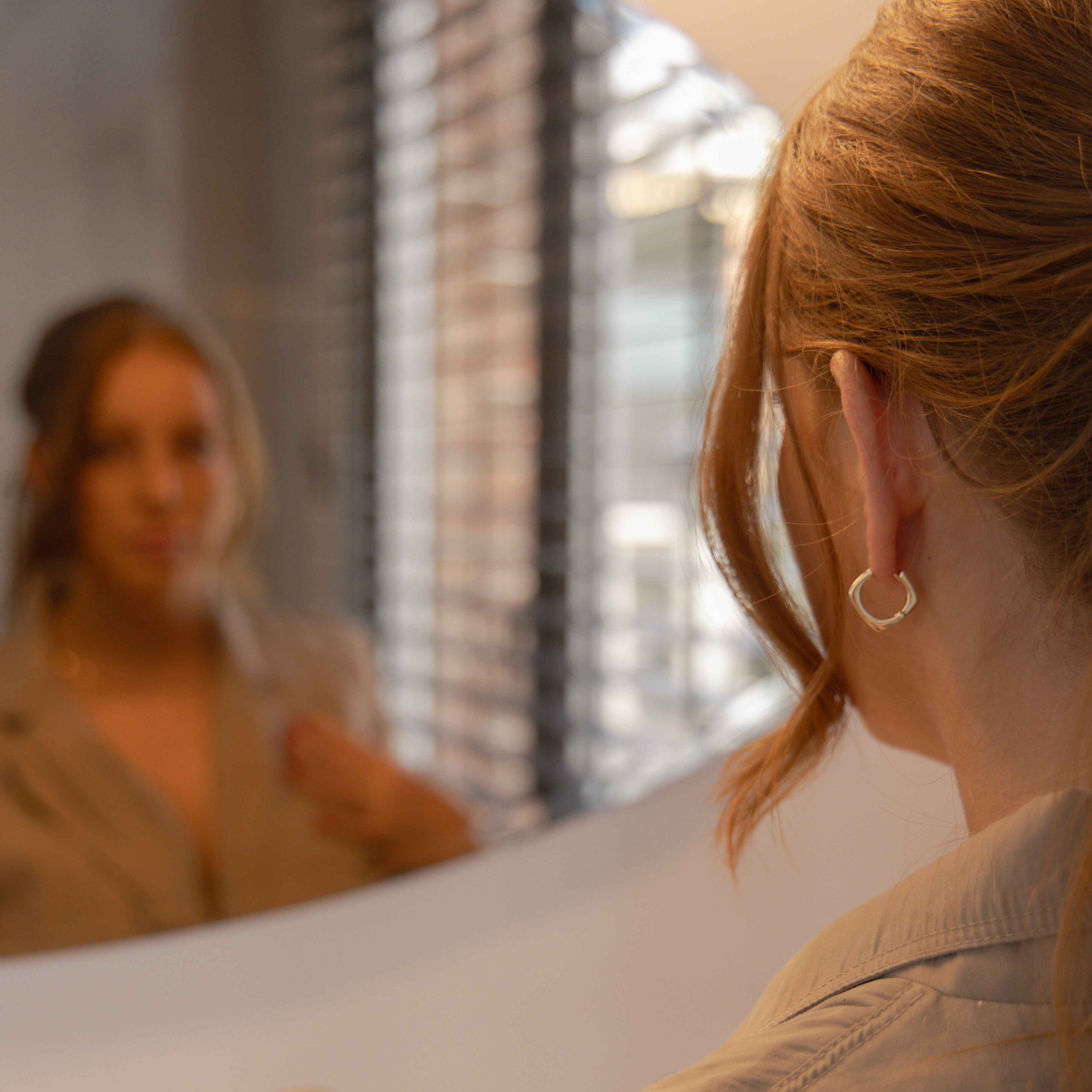 Woman standing in front of a mirror wearing gold square earrings