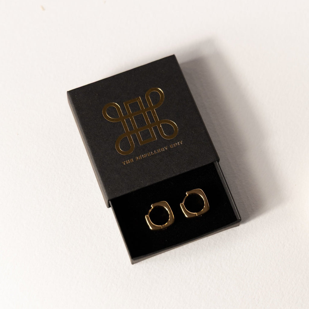 Gold hoop earrings in a black box with a brand logo on a white background