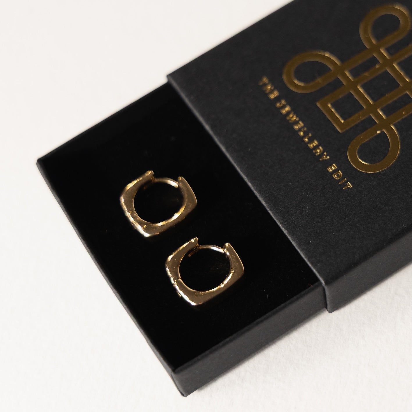 Gold hoop earrings in a black box with a brand logo on a white background
