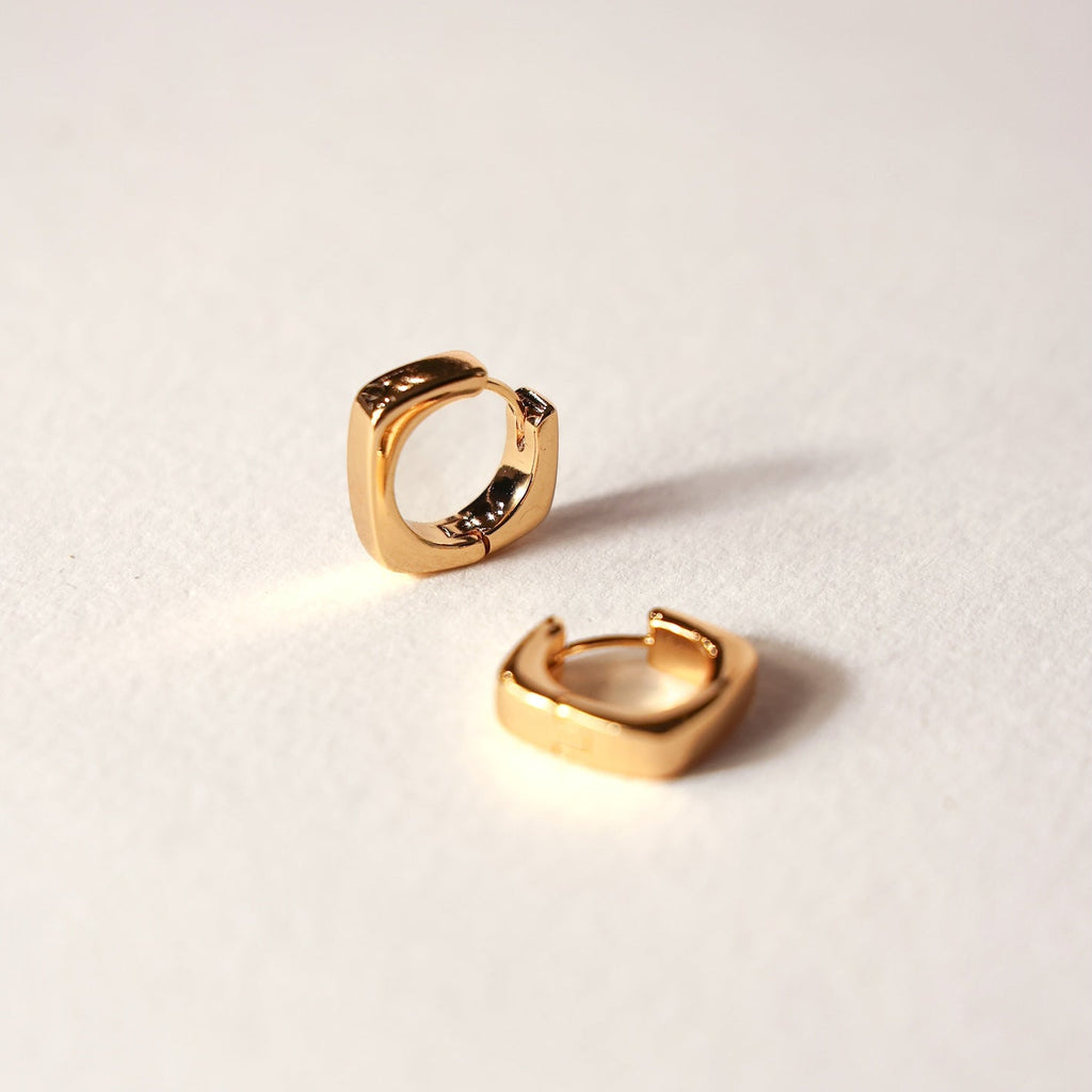 Gold square hoop earrings on a light beige background
