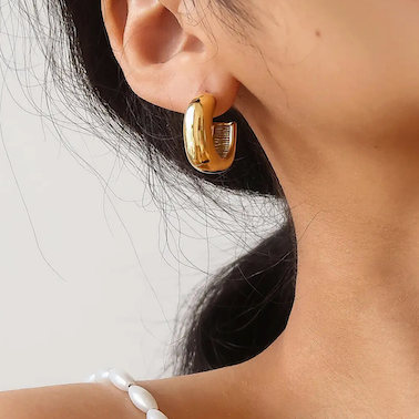Gold hoop earring worn by a woman with dark hair on a plain background