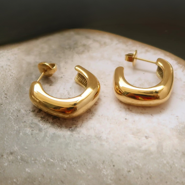 Gold hoop earrings on a textured surface with a dark background
