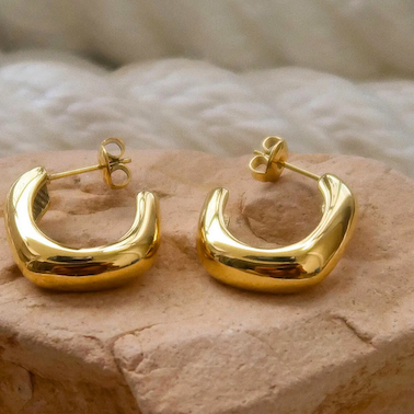 Gold hoop earrings on a textured stone surface