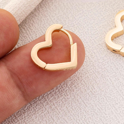 Gold heart-shaped earring on a finger with a light background