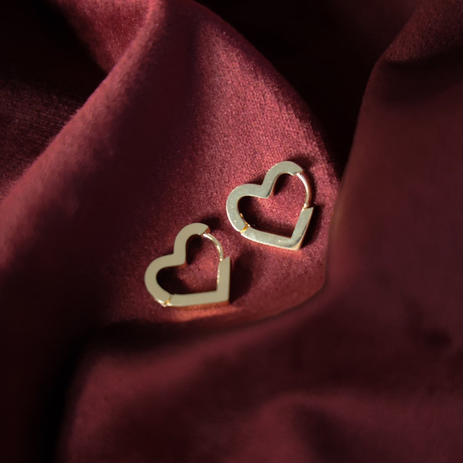 Gold heart-shaped earrings on a burgundy fabric background