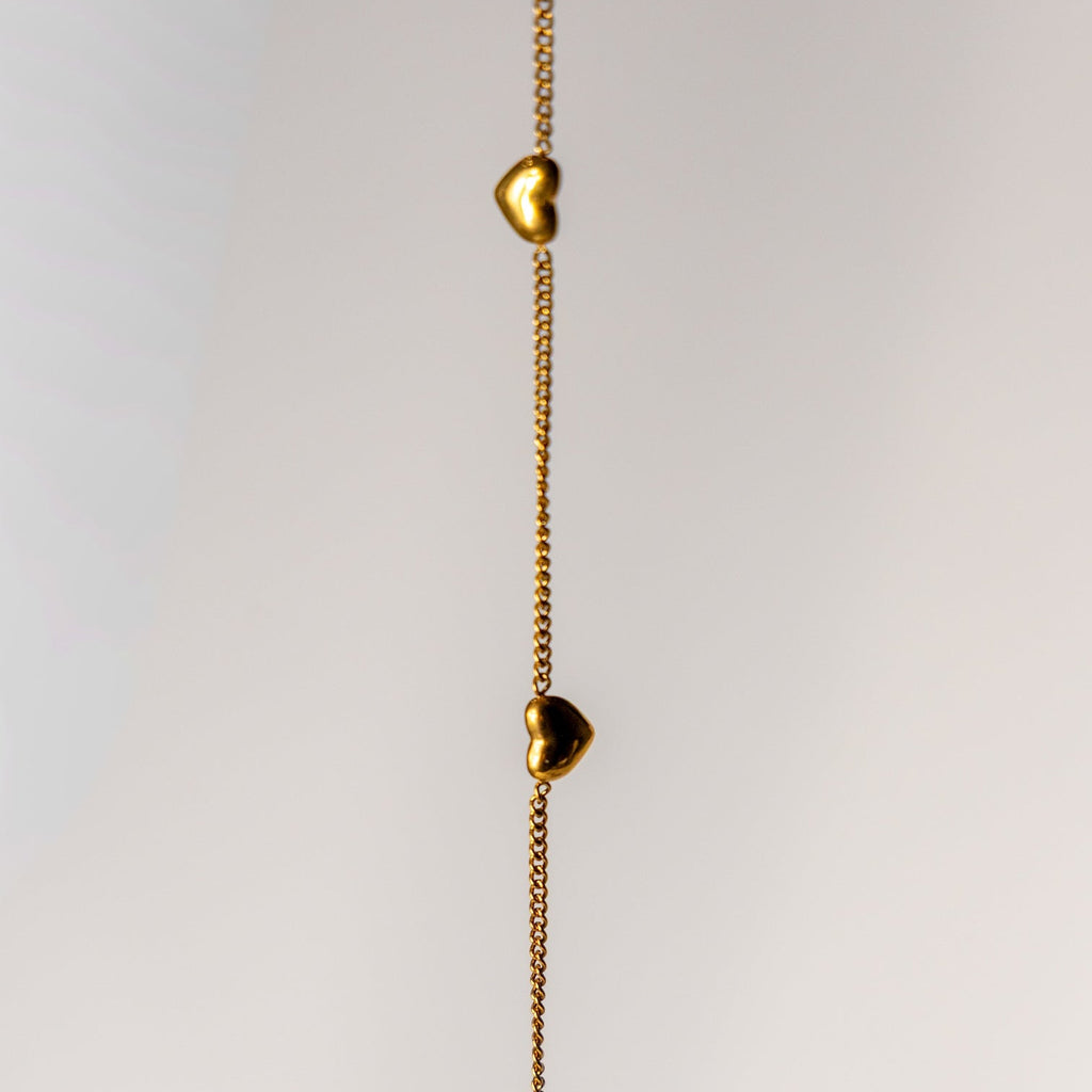 Gold necklace with heart-shaped pendants on a light gray background