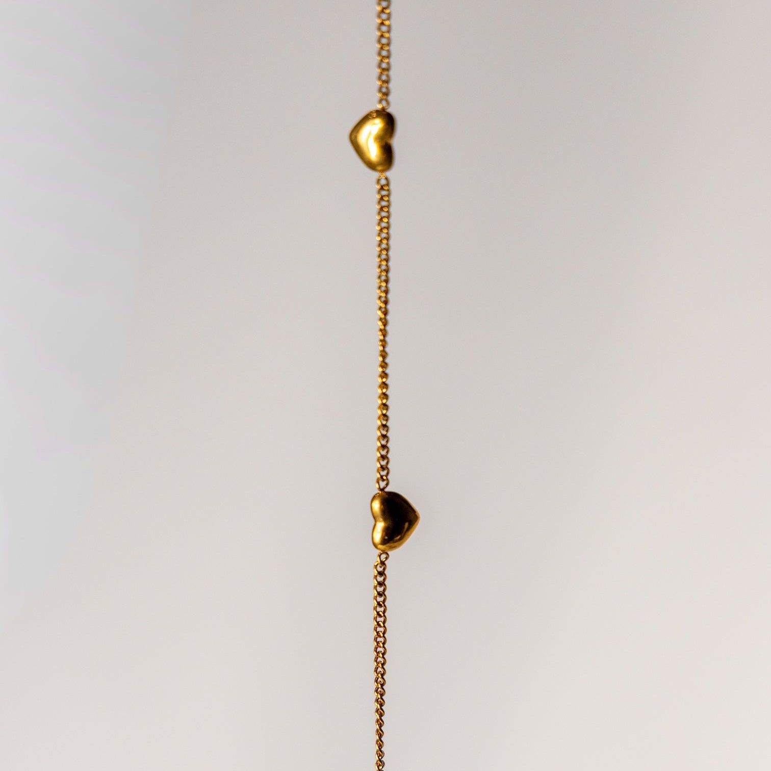 Gold necklace with heart-shaped pendants on a light gray background