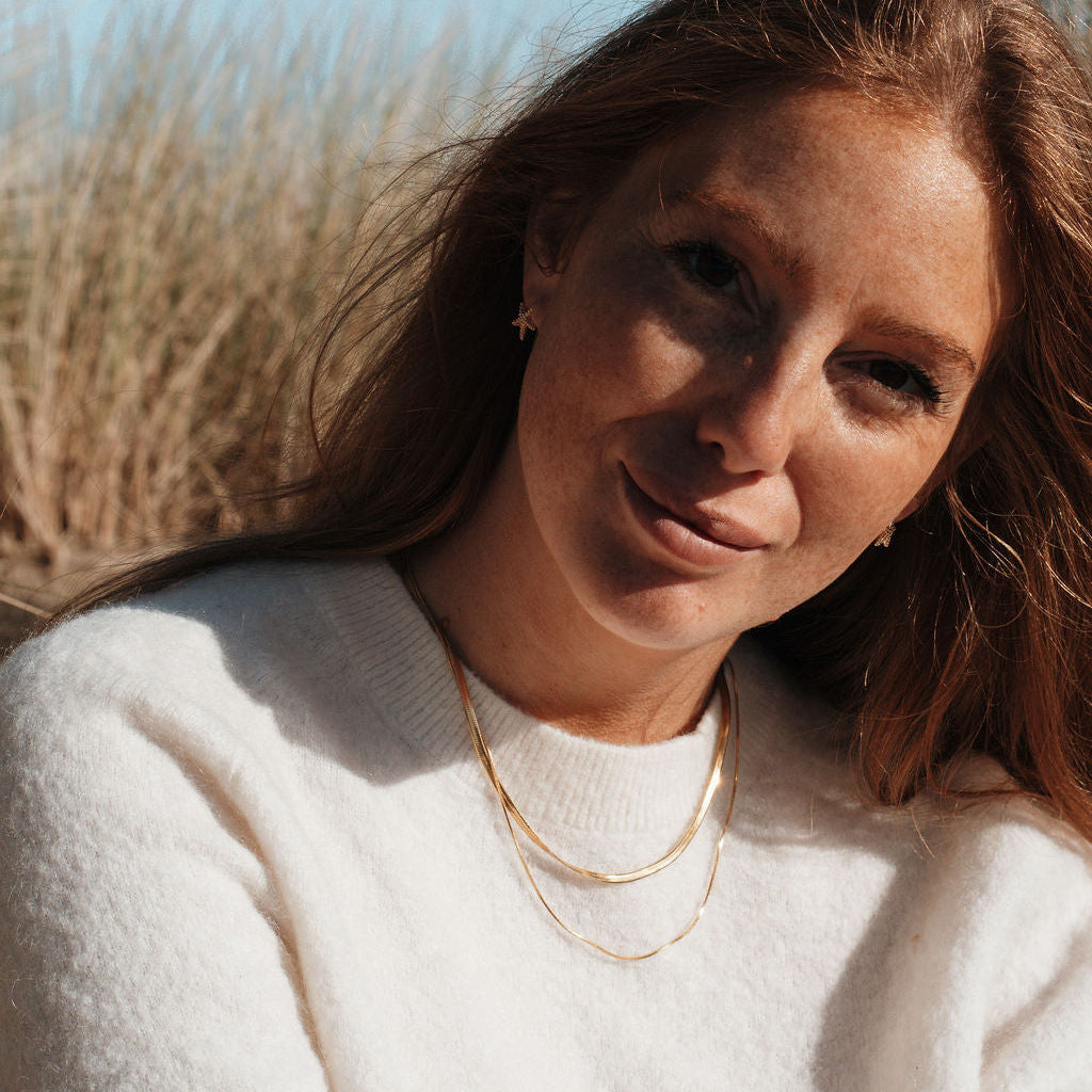 Woman outdoors with long auburn hair wearing a white jumper and gold chain necklace