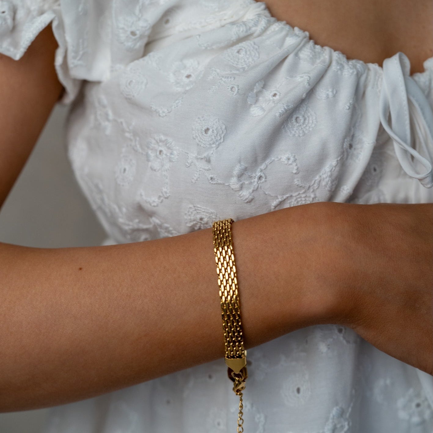 Elegant gold bracelet by the jewellery edit on a woman's wrist with a white lace top in the background