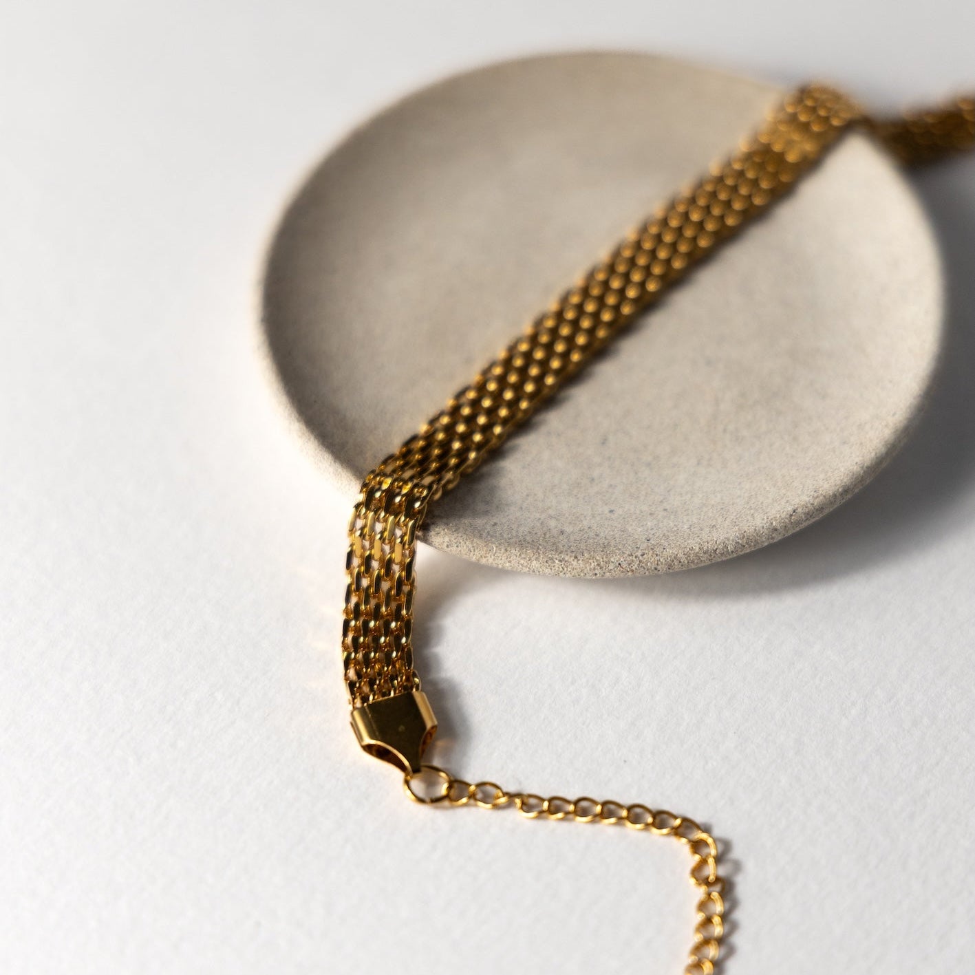 Gold chain bracelet on a white surface with a beige stone