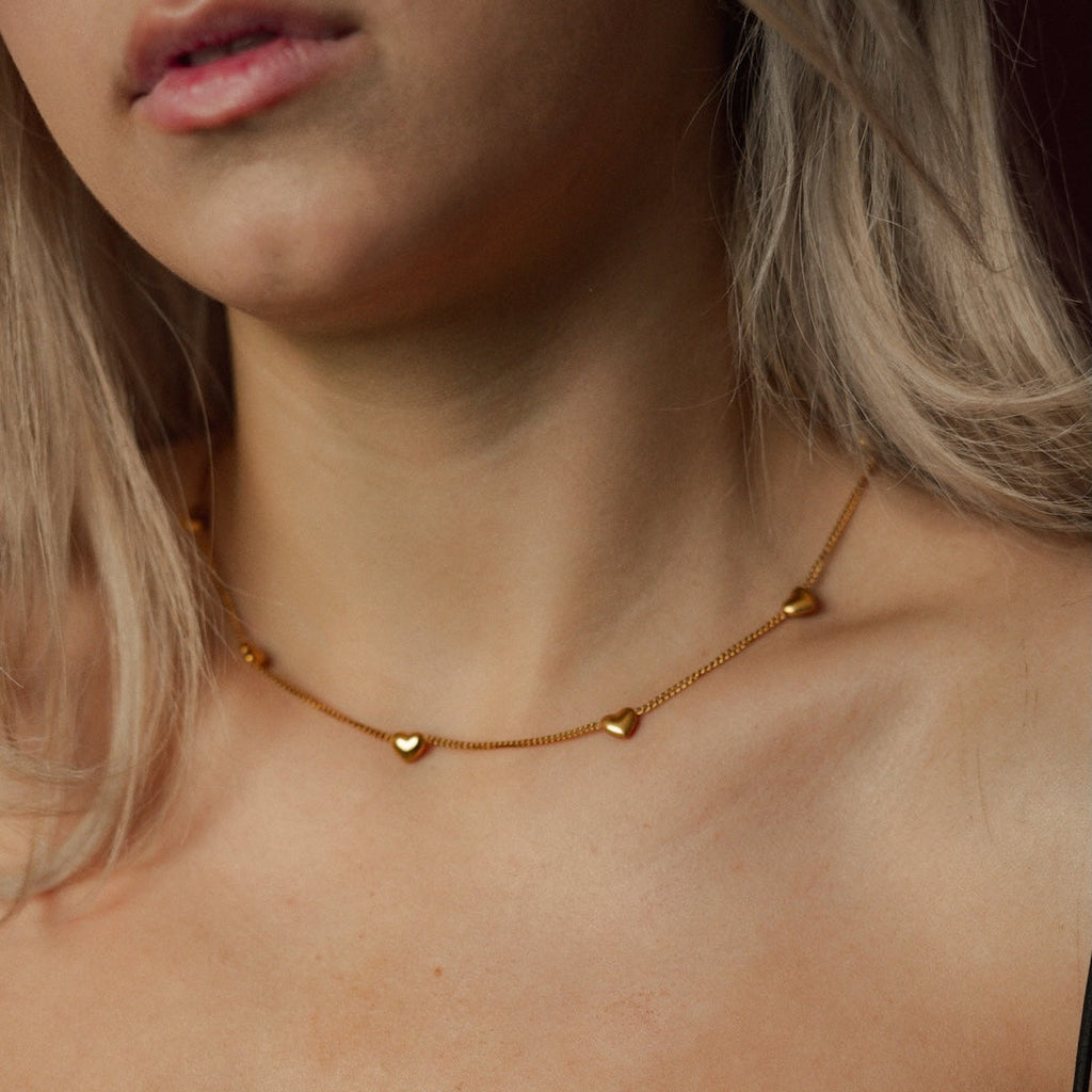 Close-up of a person wearing a gold necklace with heart pendants.