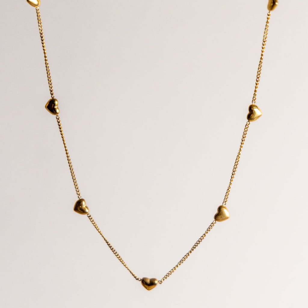 Gold necklace with small heart-shaped pendants on a light gray background
