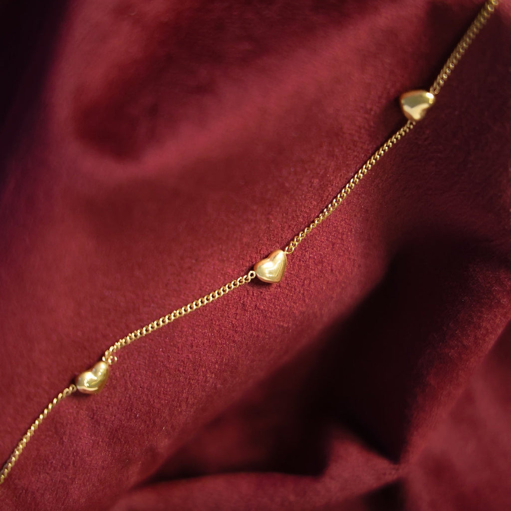 Gold heart-shaped necklace on a burgundy fabric background