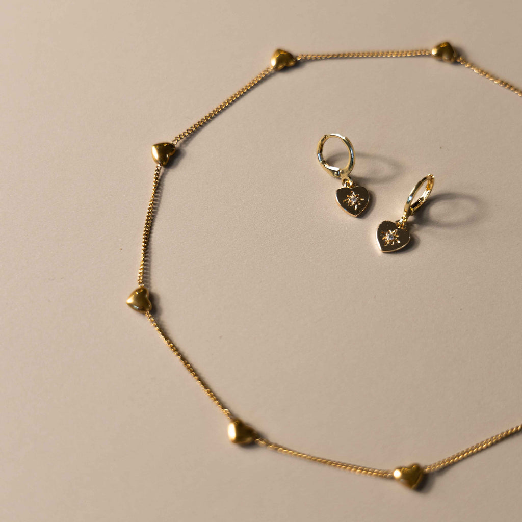 Gold heart shaped necklace and earrings on a beige background