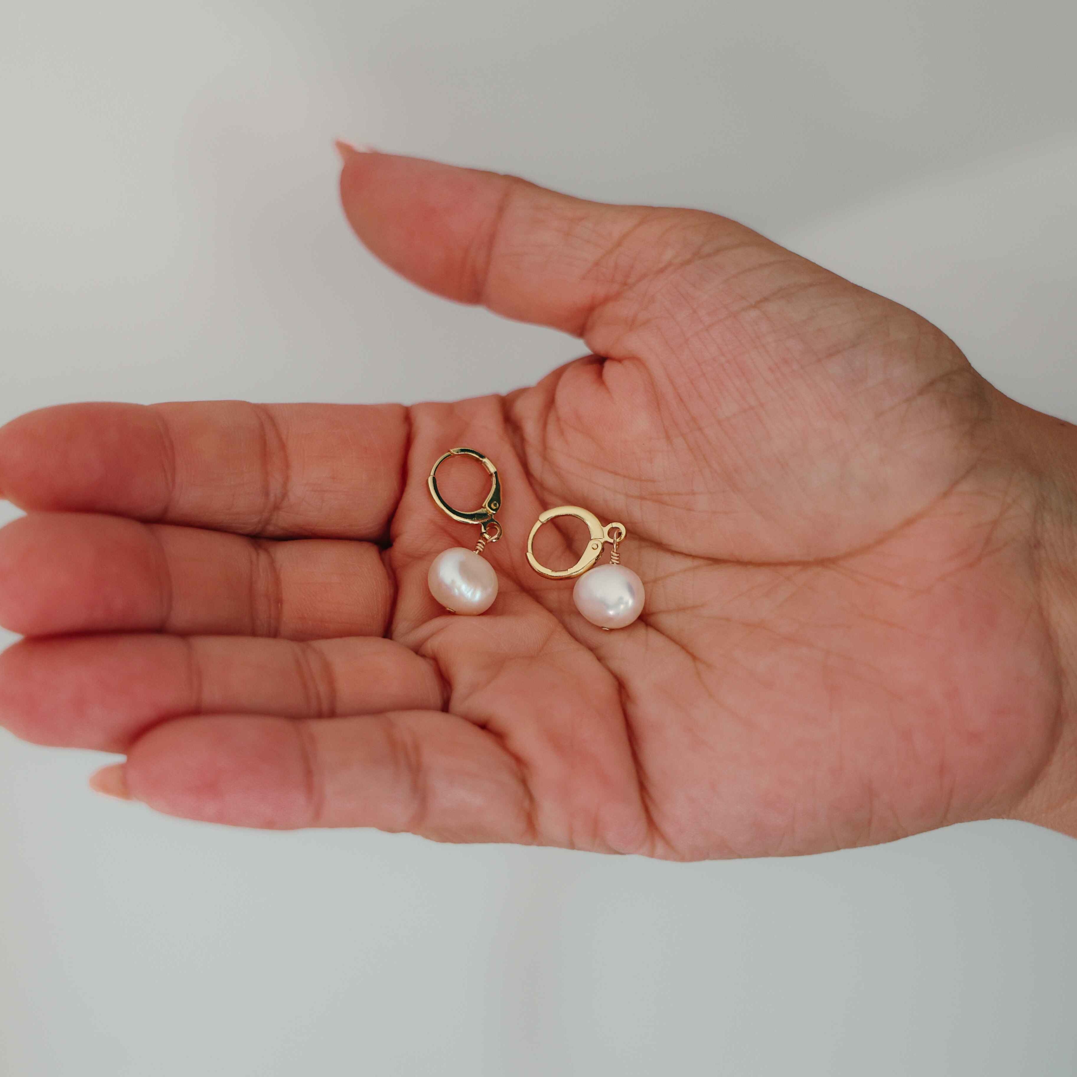 Hand holding freshwater pearl earrings against a plain background