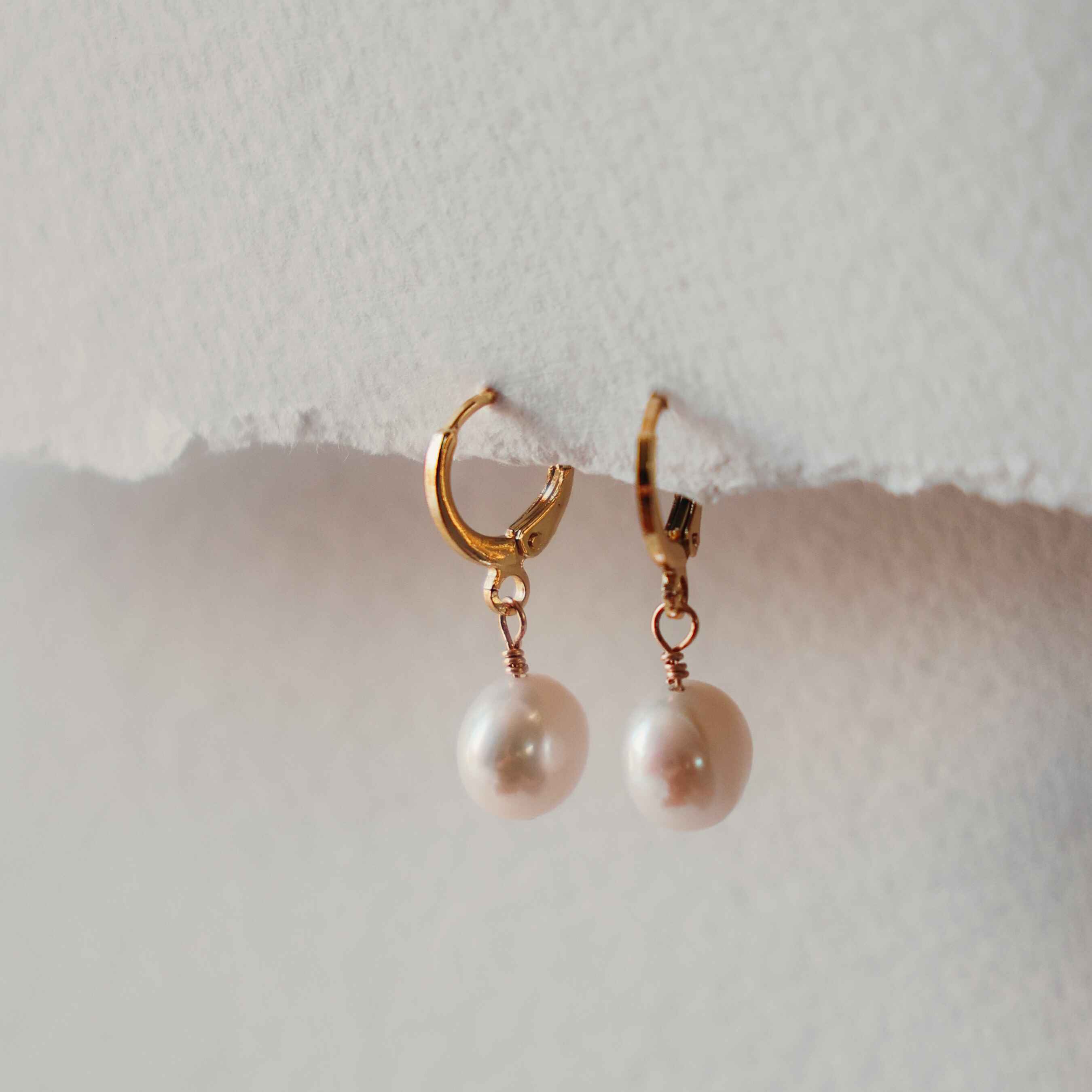 Gold hoop earrings with pearl drops on a light background
