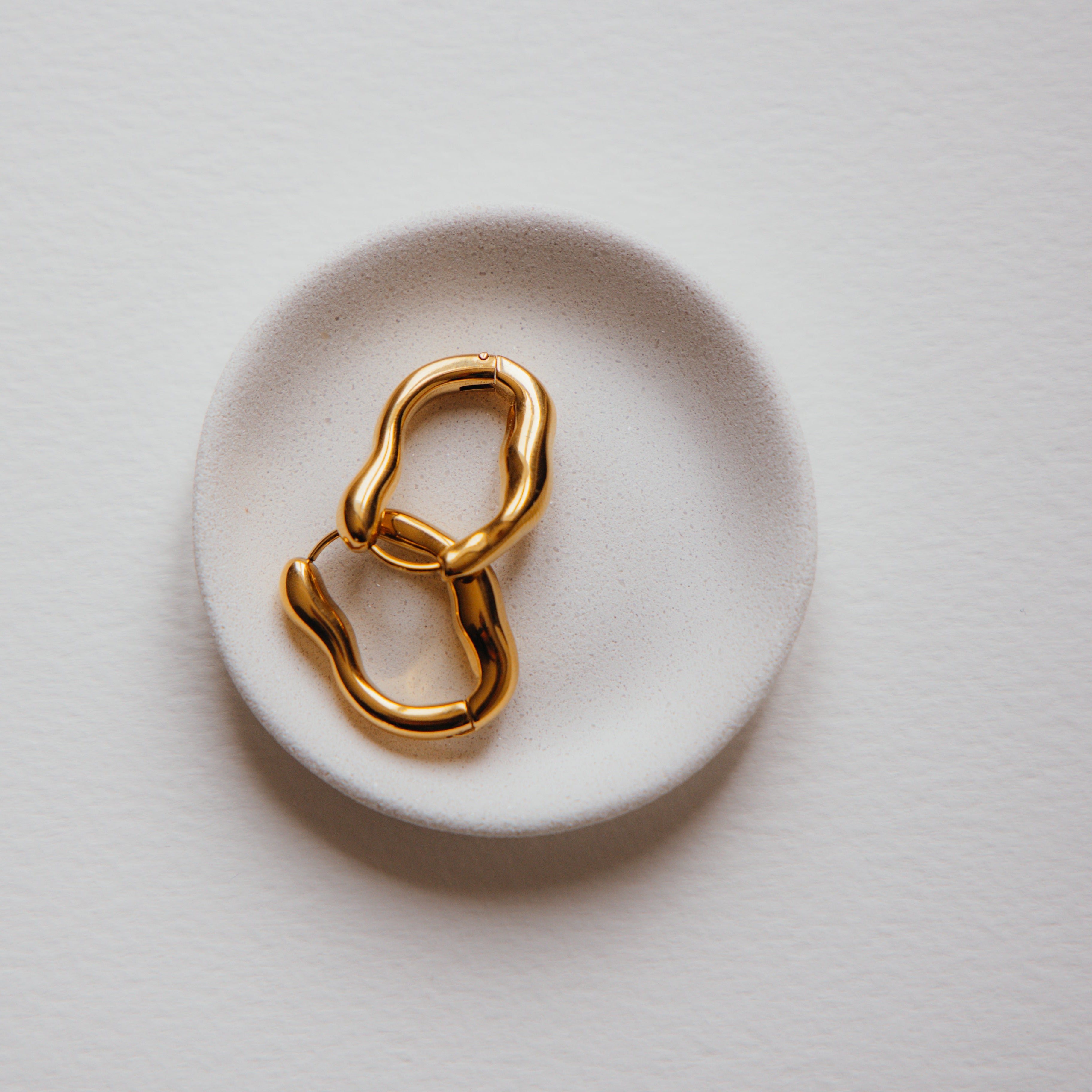 Gold earrings on a white ceramic dish with a light background