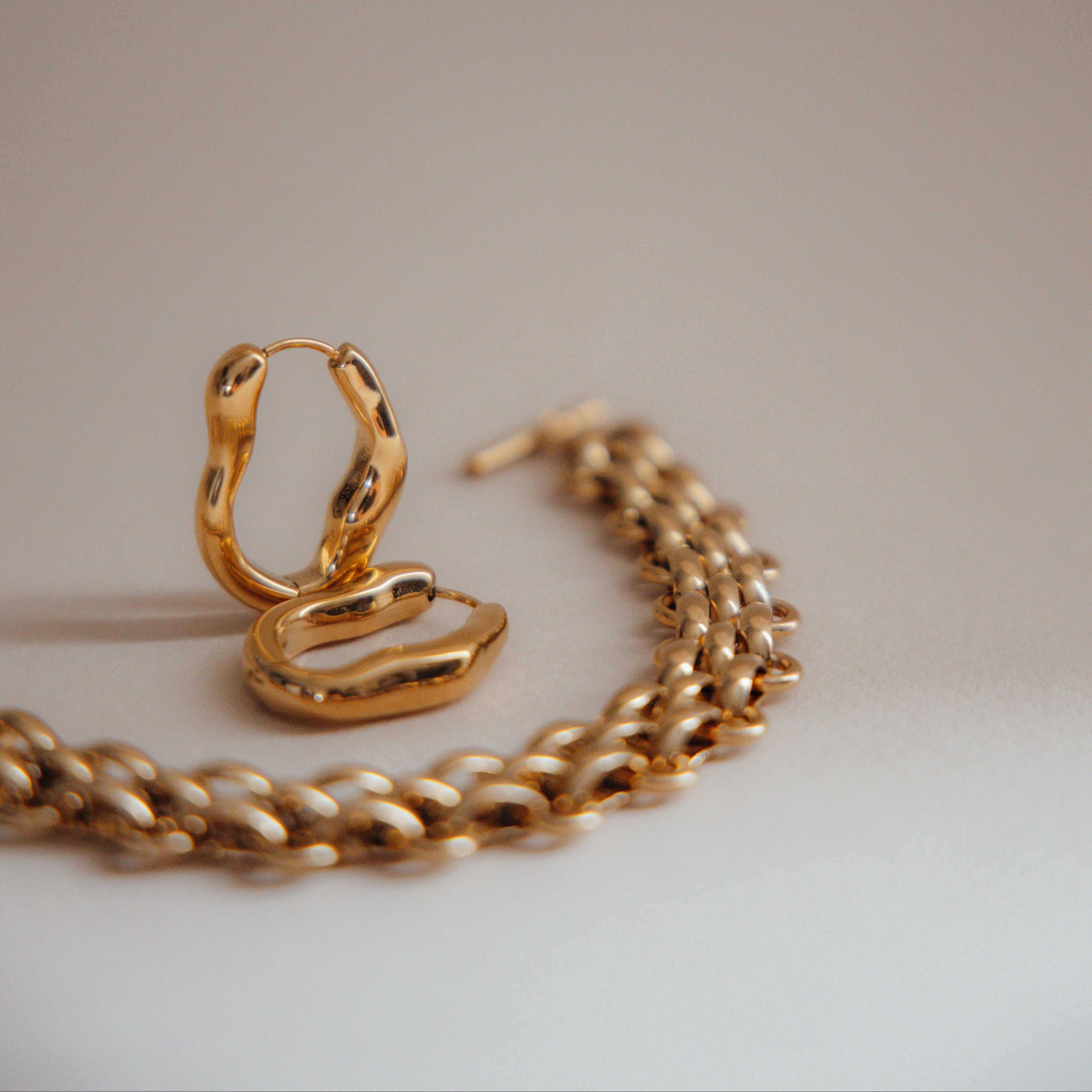 Gold earrings and chain bracelet on a neutral background