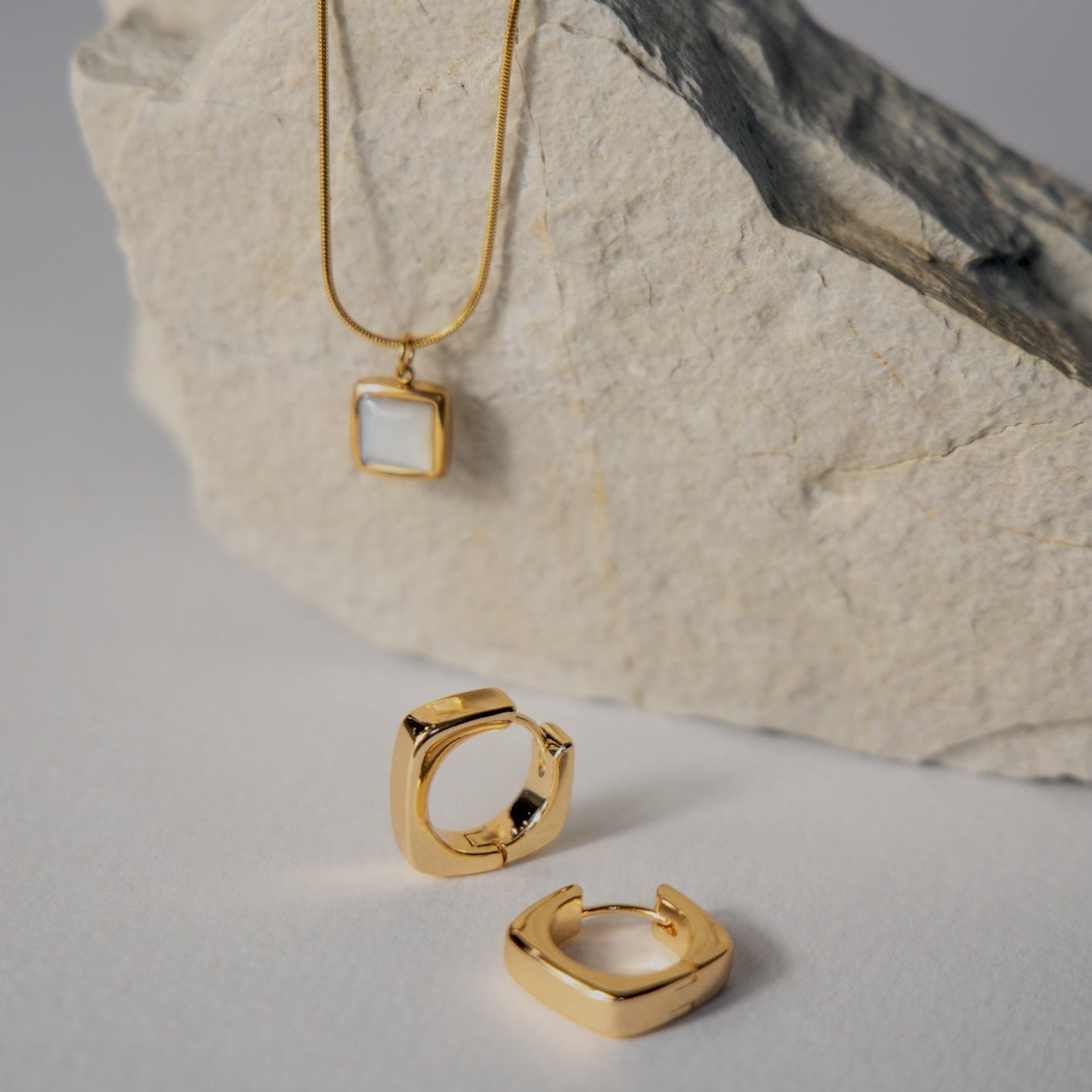 Gold necklace and earrings on a textured stone surface