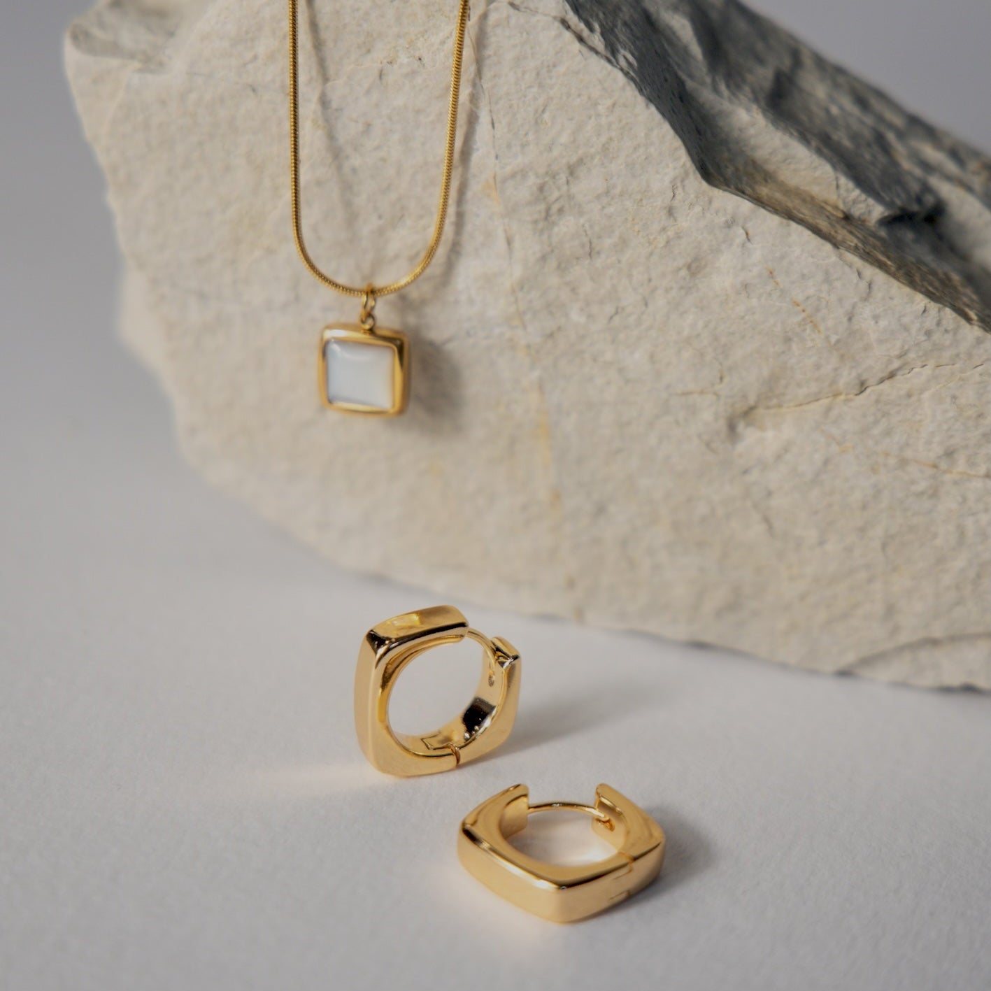 Gold necklace and earrings on a textured stone surface