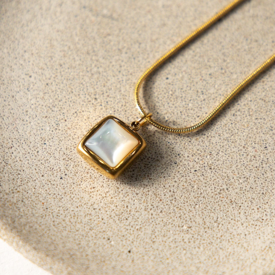 Necklace with a square pendant on a beige surface