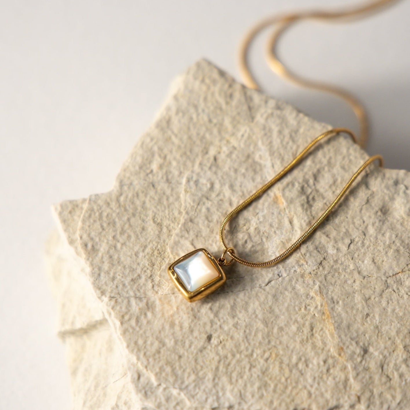 Gold necklace with a square pendant on a stone surface