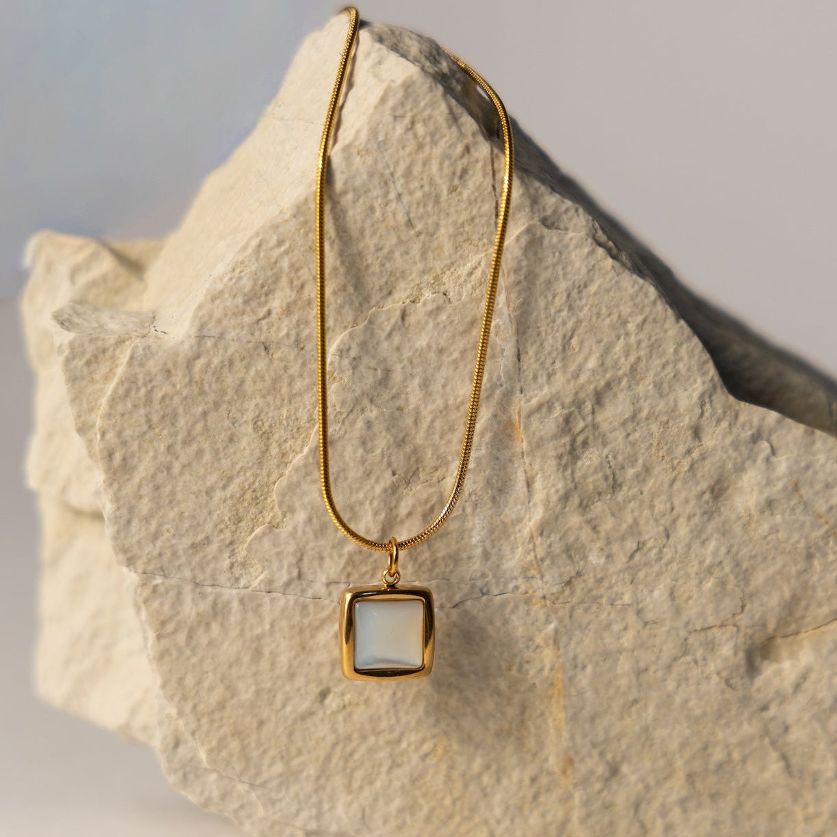 Gold necklace with a square pendant on a stone surface