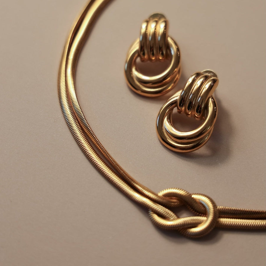 Gold hoop earrings and gold knot necklace on a beige background