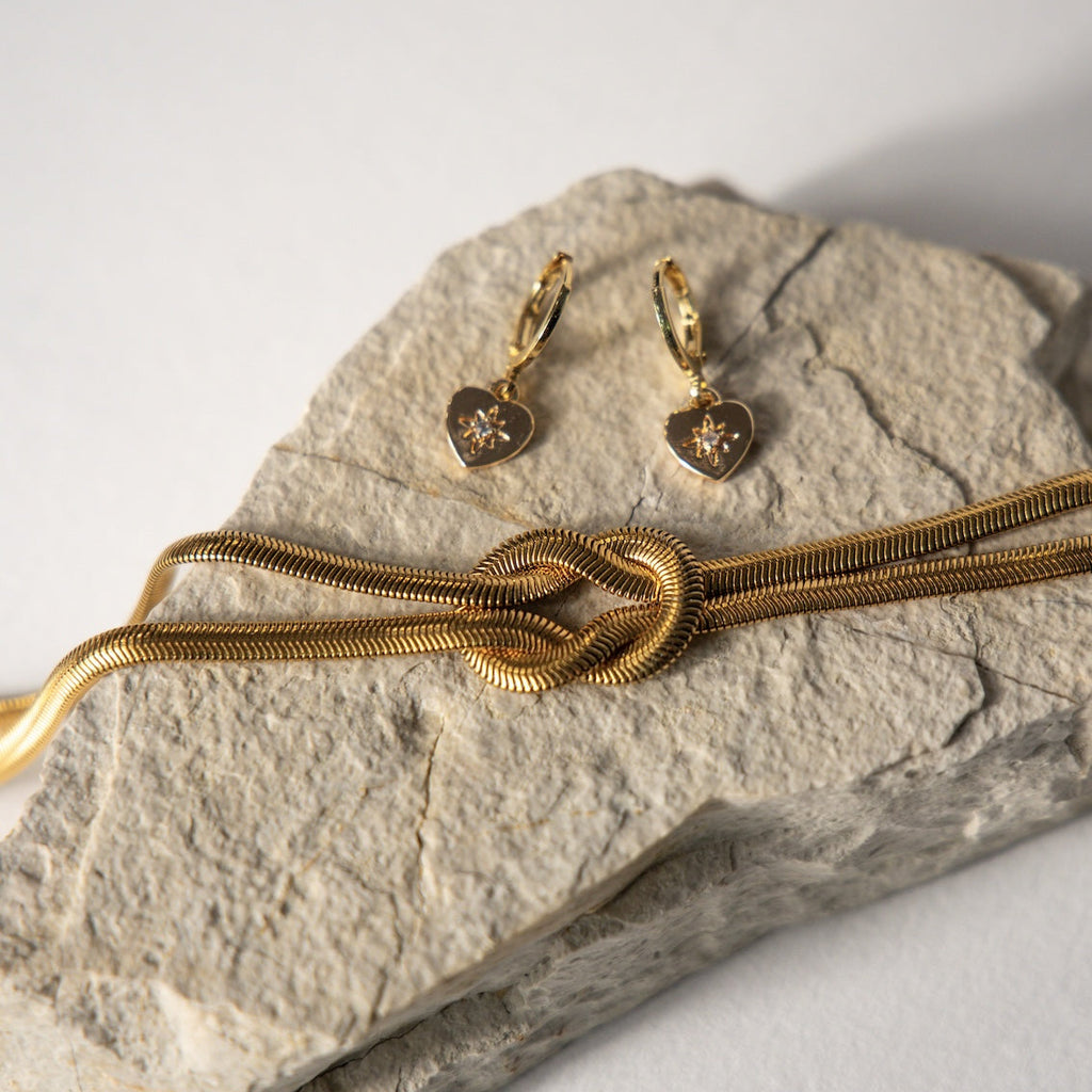 Gold necklace and earrings on a stone surface