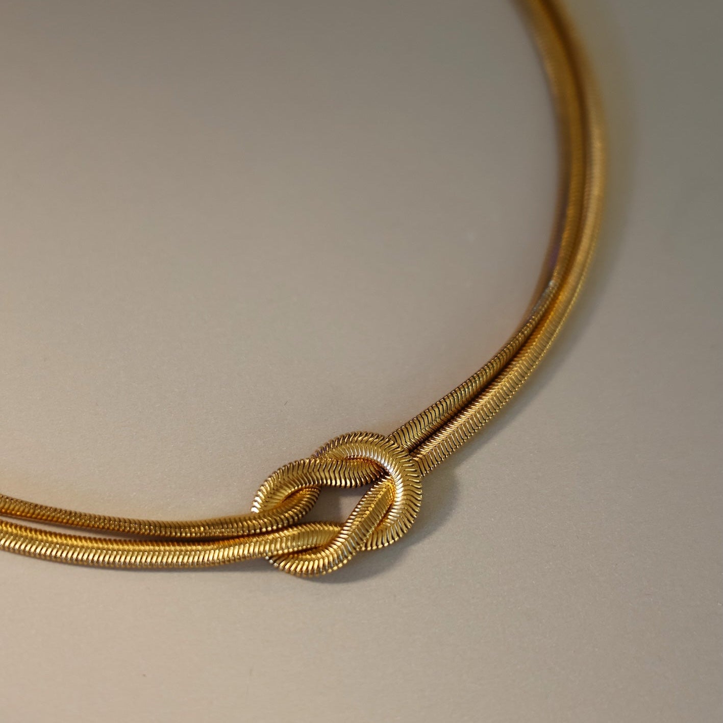Gold necklace with a knot design on a gray background