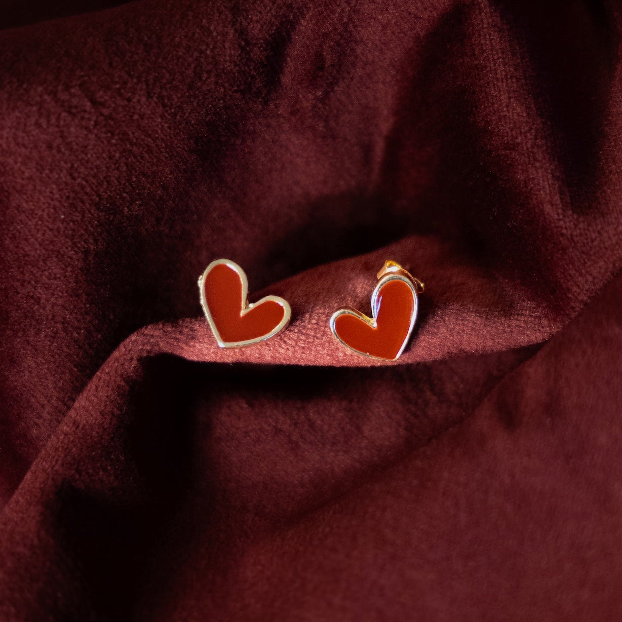Heart-shaped earrings on a maroon fabric background