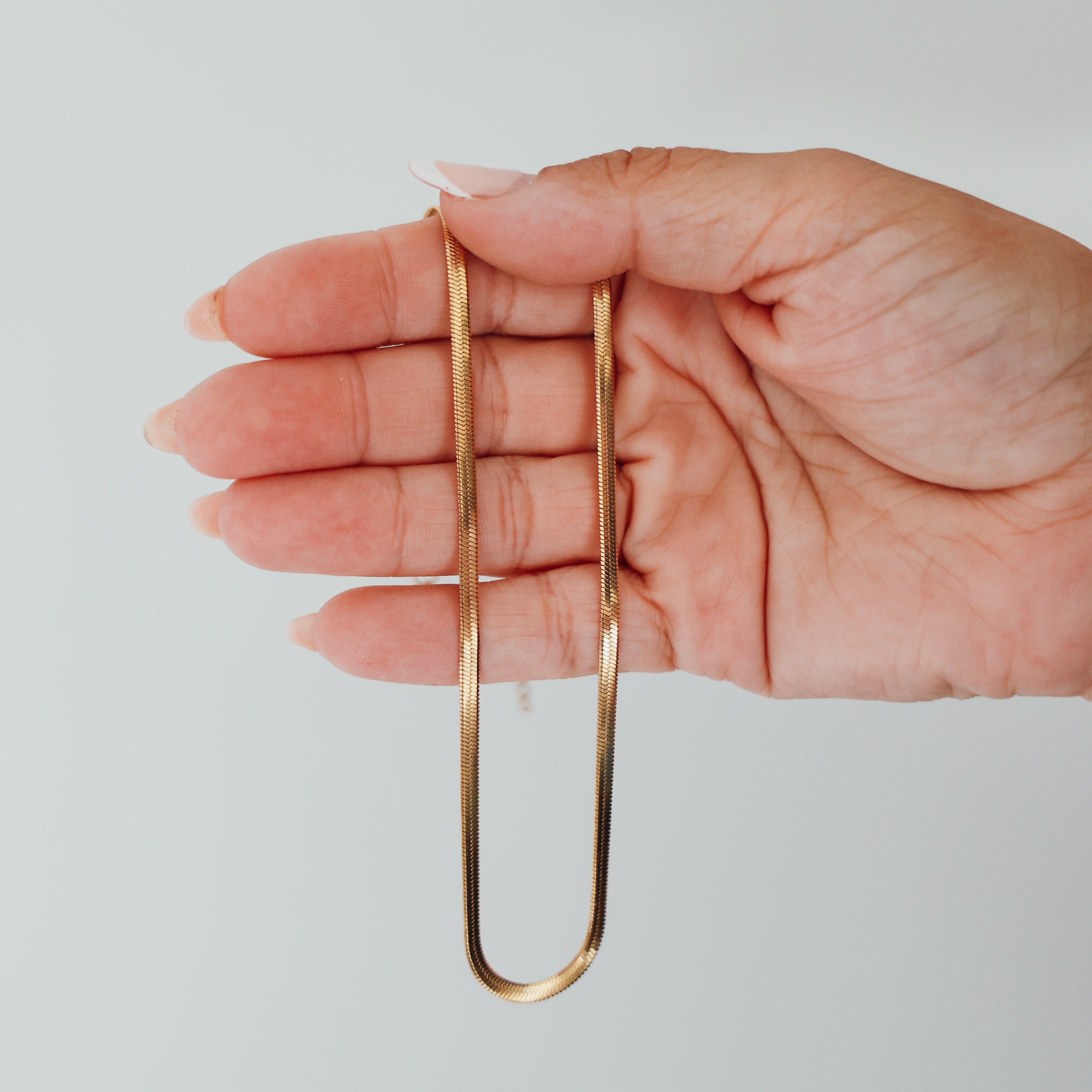Hand holding a hypoallergenic 18k gold elegant bracelet against a plain background