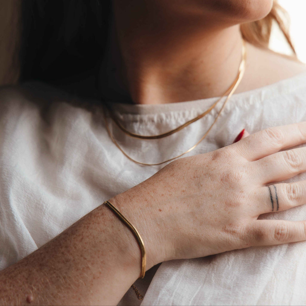 Close-up of a person wearing a gold bracelet and necklace with a white shirt.