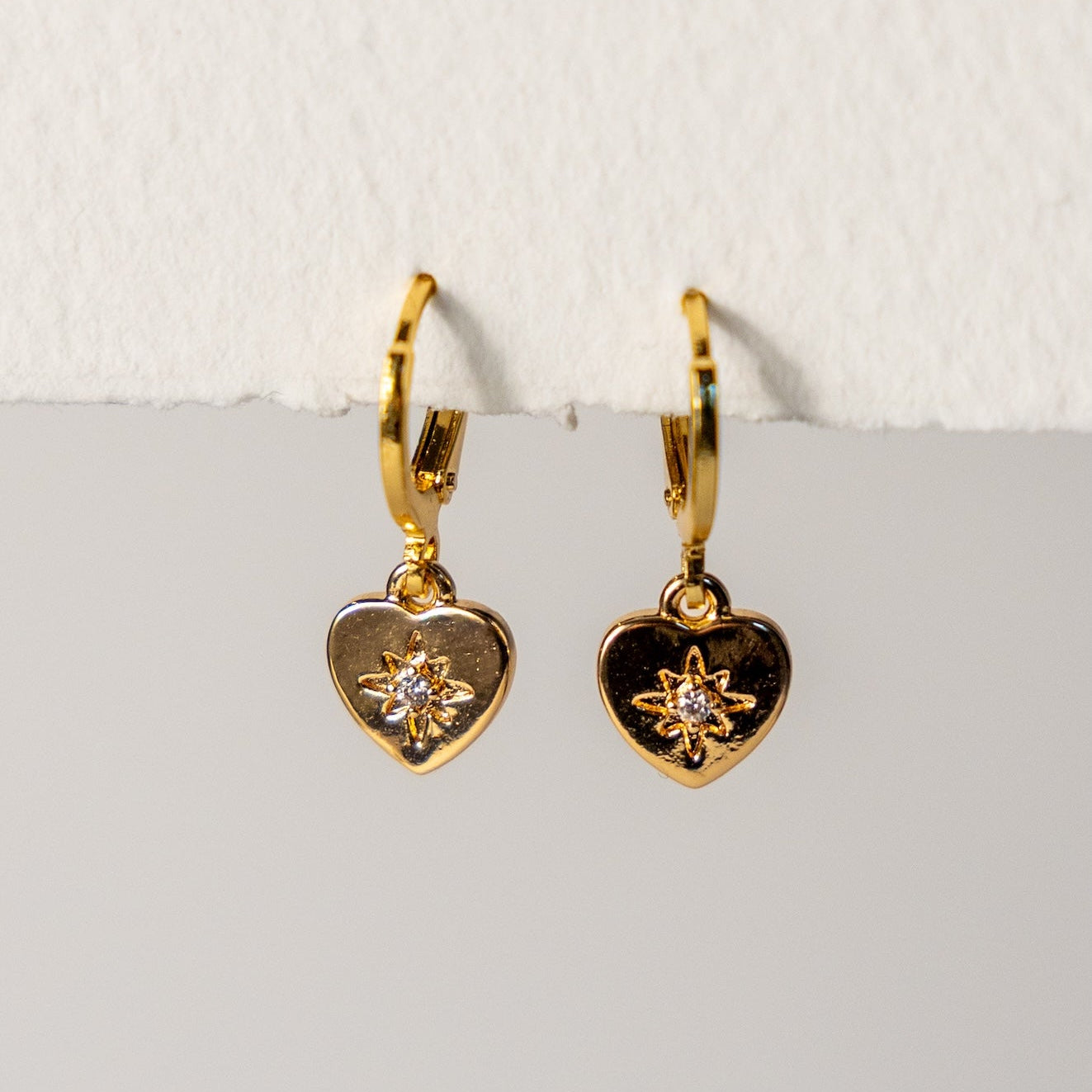 Gold heart-shaped earrings with star designs on a light gray surface.