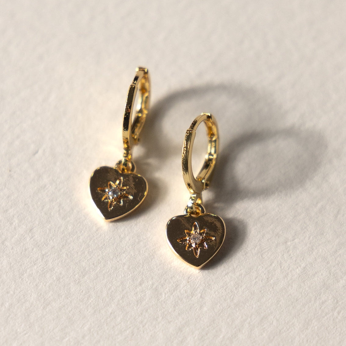 Gold heart-shaped earrings with embedded stones on a light gray background