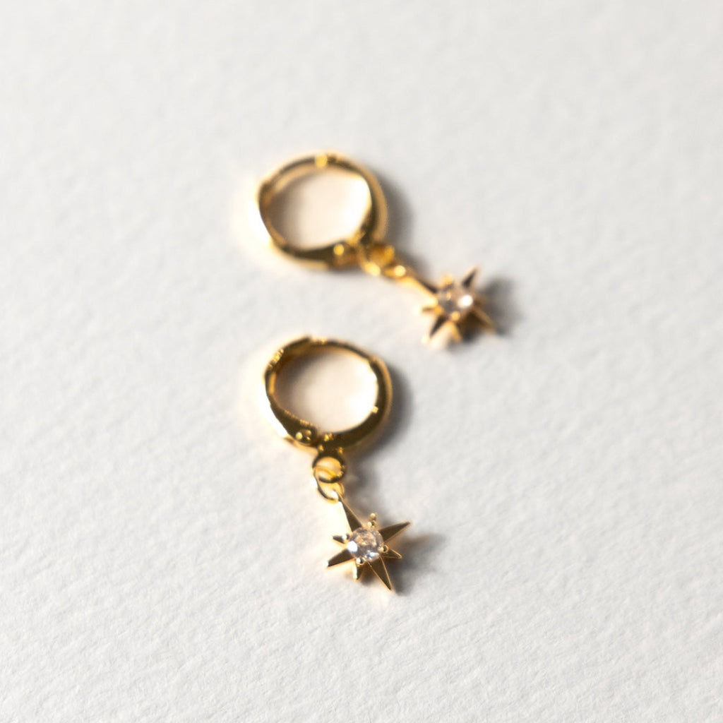 Gold hoop earrings with star-shaped charms on a light gray background