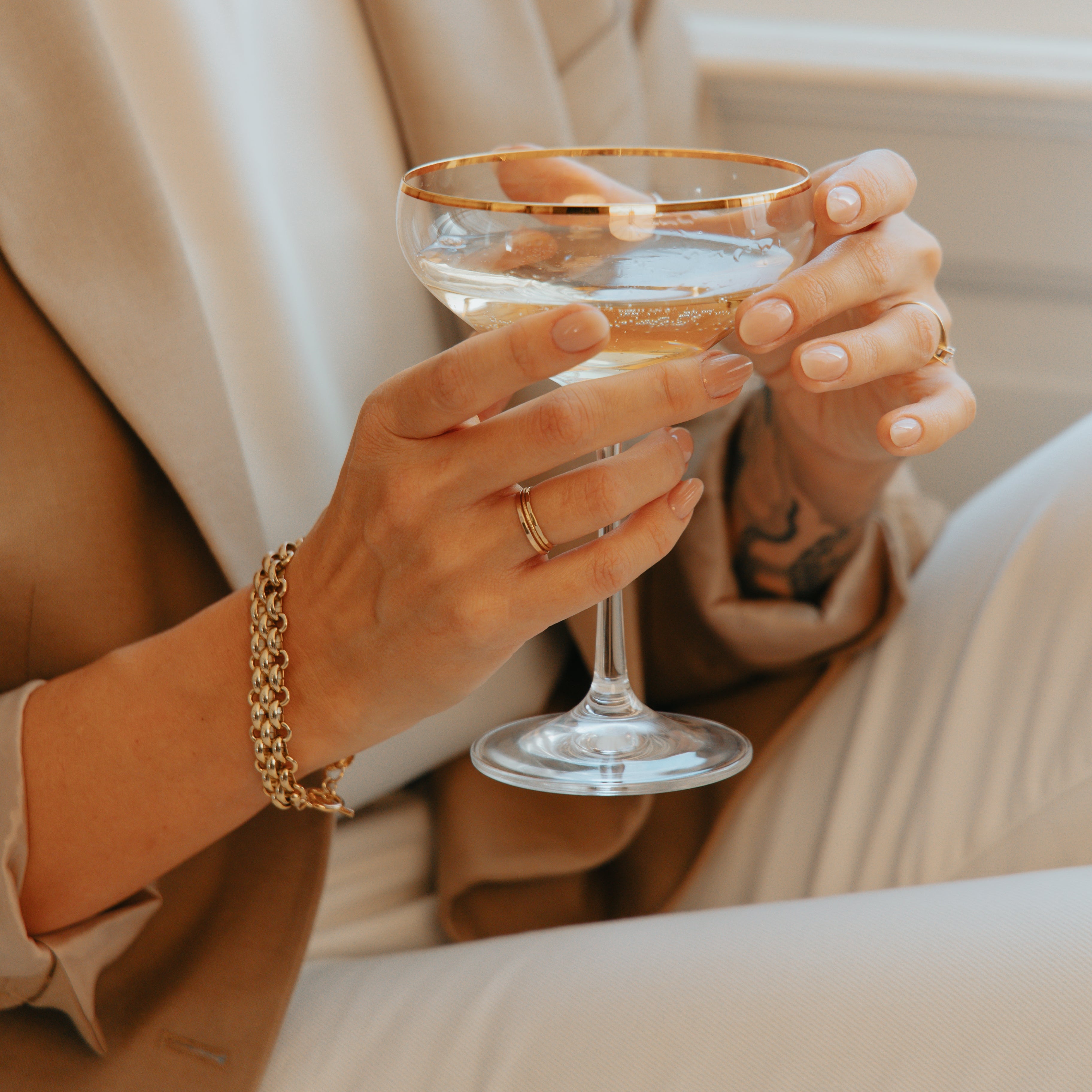 Person wearing s gold bracelet holding a glass with a neutral background