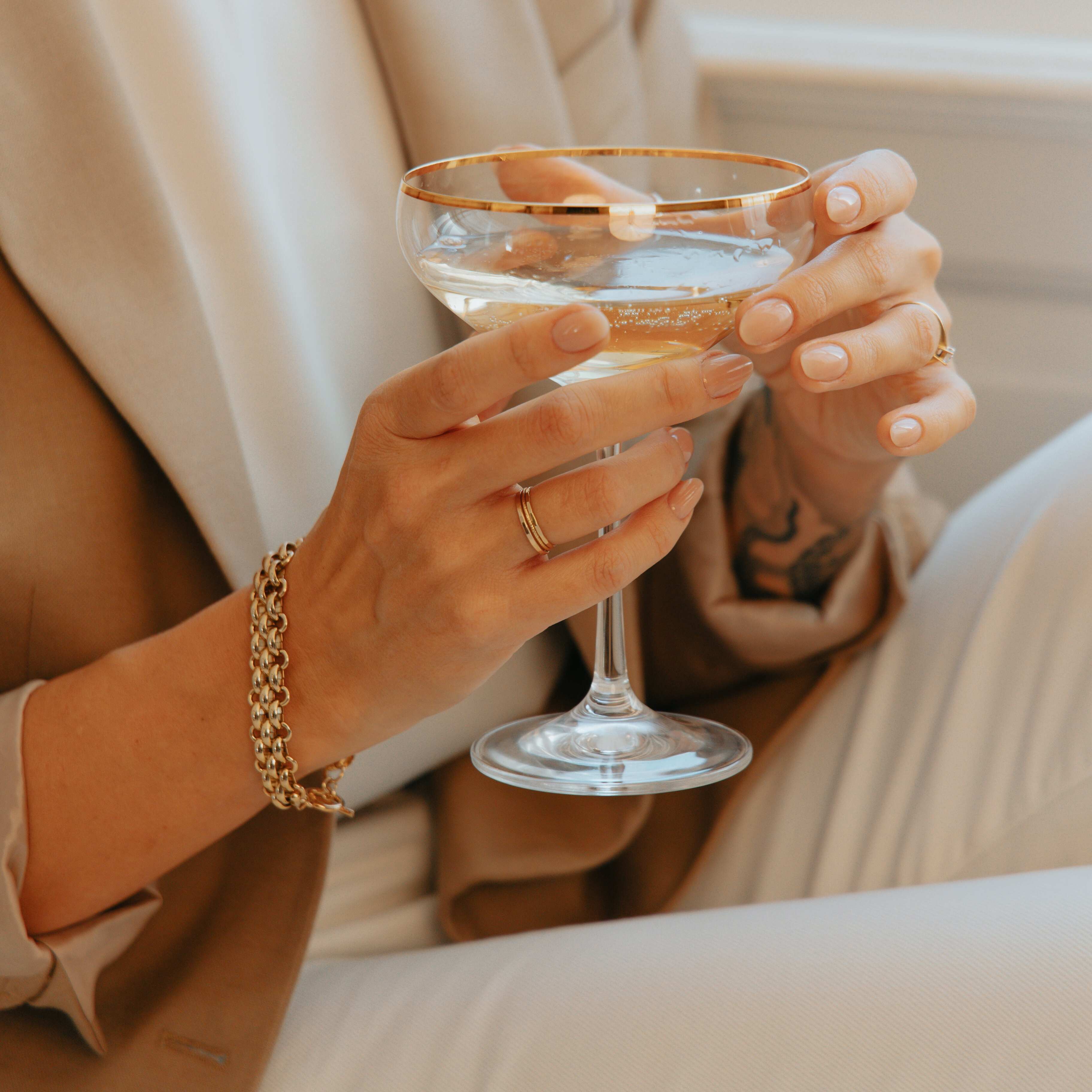 Person wearing s gold bracelet holding a glass with a neutral background
