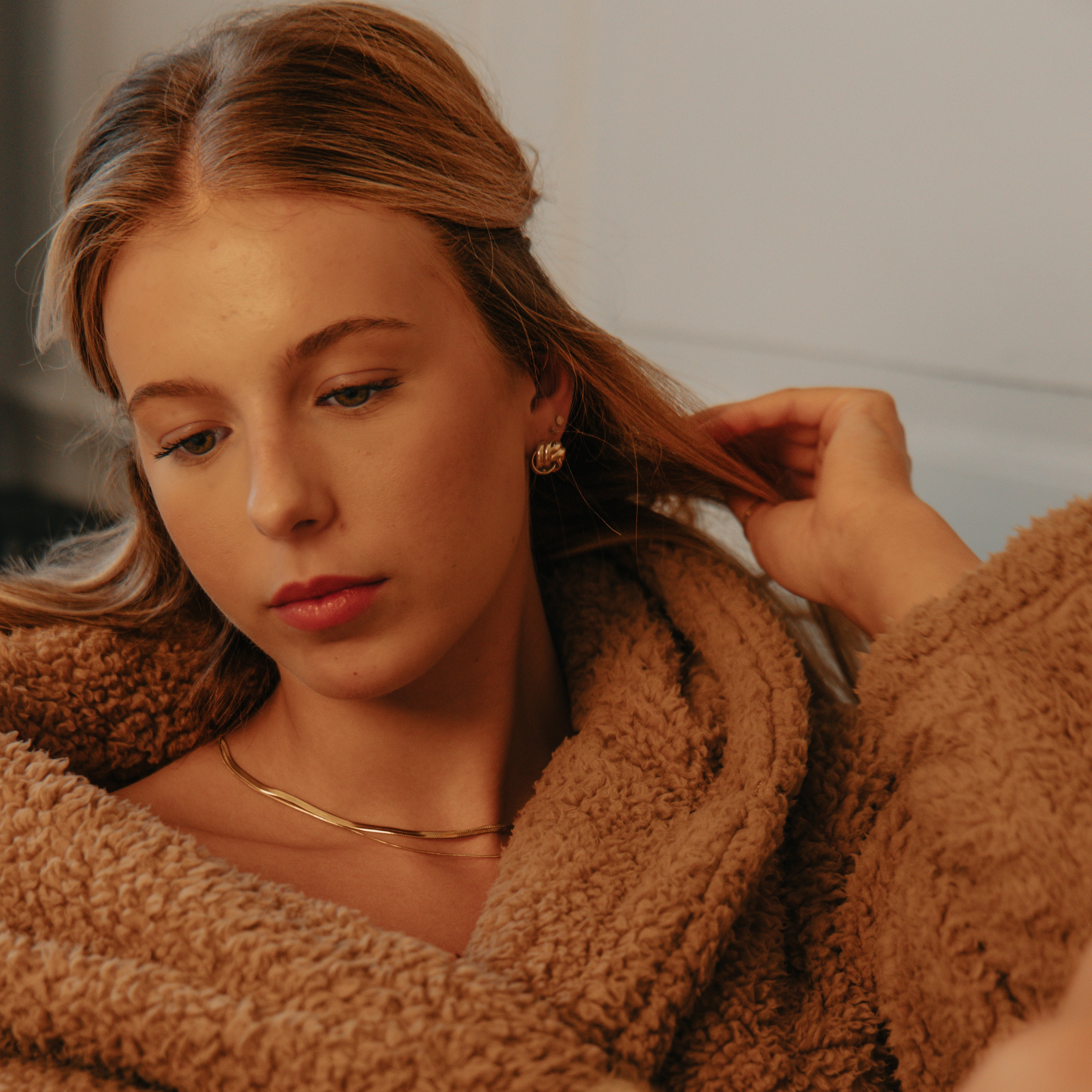 Woman in a brown robe and gold jewellery holding a book, with a warm and cozy atmosphere.