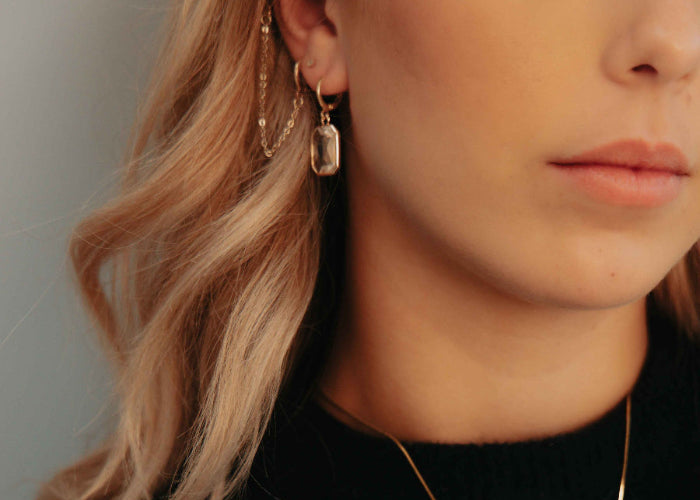Close-up of a person wearing gold earrings and a necklace against a neutral background