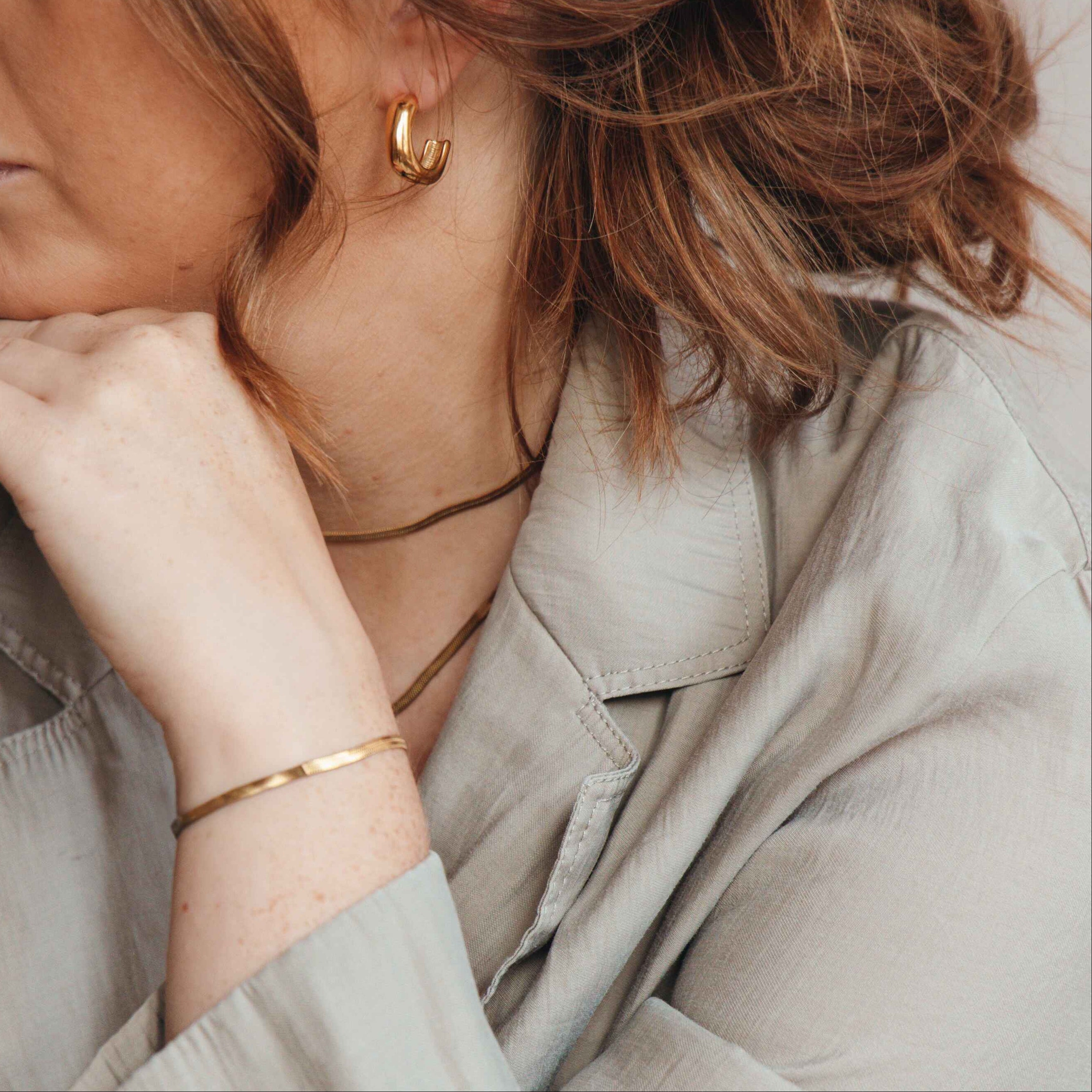 Woman wearing gold earrings and a bracelet, with a neutral background