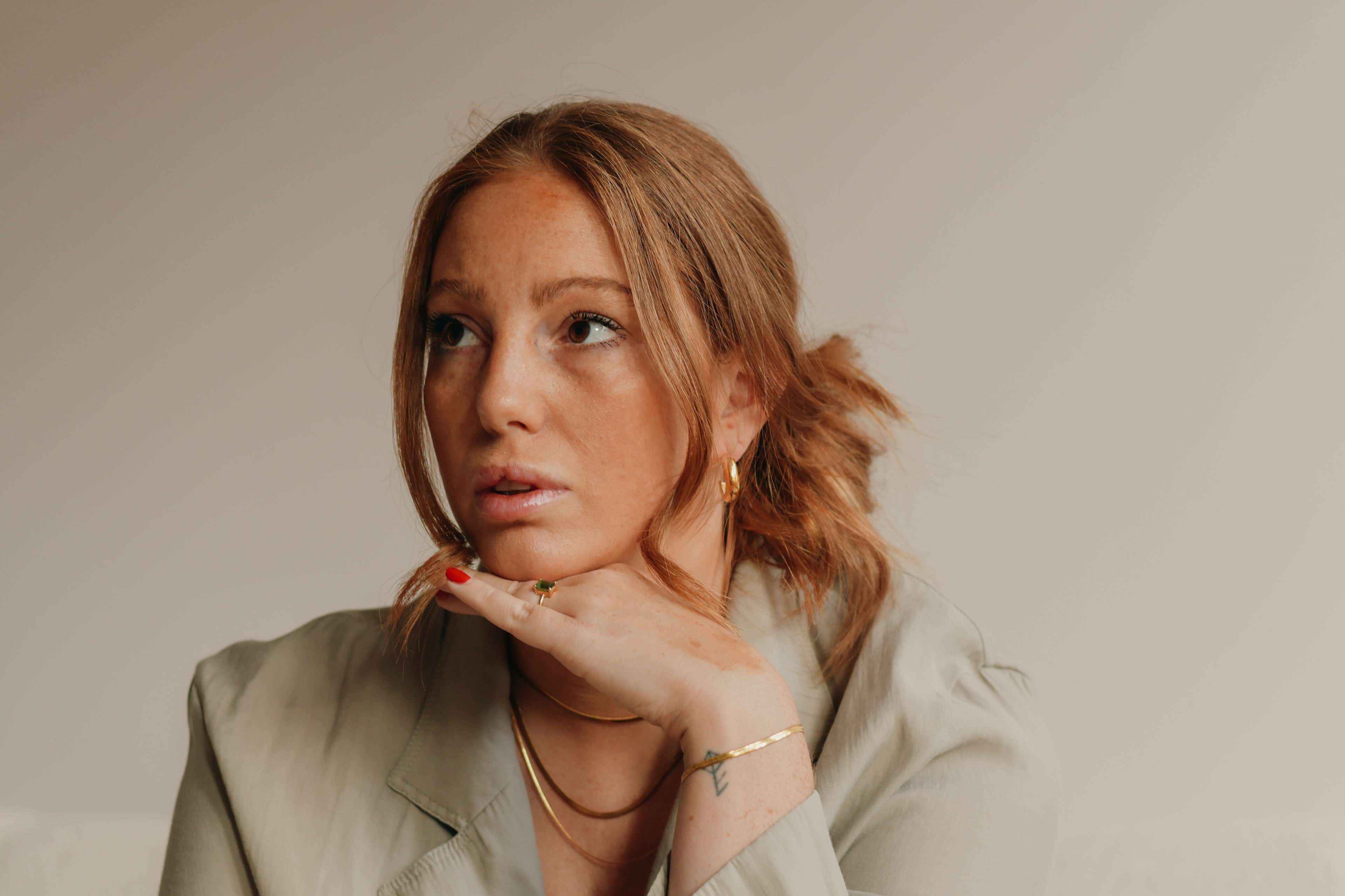 Woman with light brown hair wearing a green blazer and gold jewellery against a neutral background