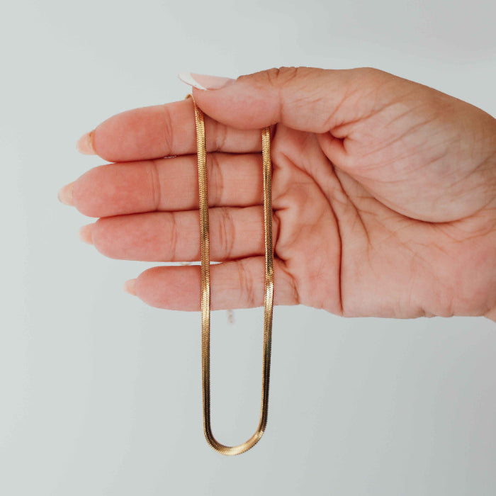 Hand holding a gold snake chain necklace against a plain background